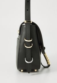 Borsa a tracolla in pelle nera vista di lato con cinturino regolabile, caratterizzata da anelli in metallo dorato e argentato e piccoli piedini protettivi in metallo alla base.