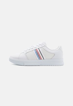 Hvid lavtop sneaker med tekstureret sidepanel og blå, rød, sort og hvid stribet detalje langs siden.