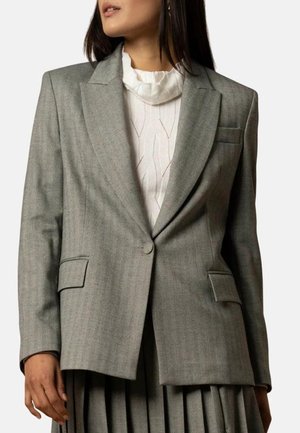 Blazer grigio su misura con reverse a punta, due tasche frontali e una trama sottile, indossato sopra un top bianco a coste.