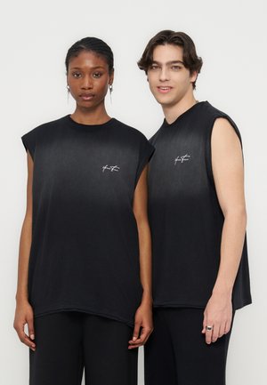 Twee modellen staan naast elkaar en dragen zwarte mouwloze tops met kleine witte logo's op de borst tegen een effen lichte achtergrond.