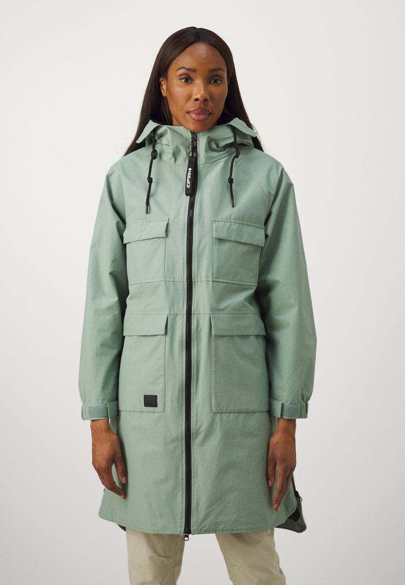 Parka longue vert clair avec fermeture éclair à l'avant, capuche ajustable et quatre poches avant. Présente un tissu texturé et un accent logo noir.