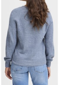 Ljusblå tröja i mjukt, texturerat material med rund hals, långa ärmar och ribbat avslut. Matchas med ljusblå jeans.