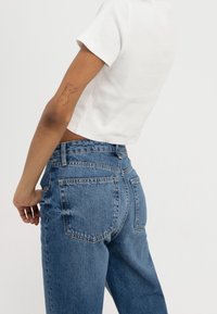Light blue denim jeans with a high waist, straight leg, and two back pockets. Paired with a fitted white short-sleeve top.