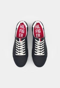 Marineblauwe canvas sneakers met witte veters, met een rode binnenzool met het "HILFIGER" logo en witte en rode strepen op de hiel. Rechte neusontwerp.
