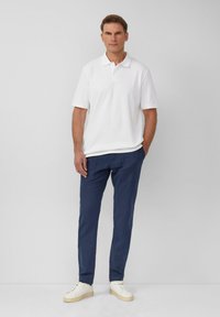 Biała koszulka polo, niebieskie spodnie i białe sneakersy. Luźny krój, krótkie rękawy, teksturowany materiał. Prosty design, bez widocznych wzorów lub logo.
