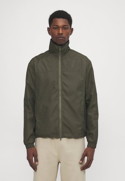 Veste légère olive avec un col haut, fermeture éclair et poignets élastiques. Texture lisse, design minimaliste et sans motifs visibles.
