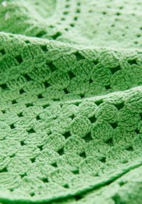 Groene gebreide stof met een gestructureerd, ingewikkeld patroon van in elkaar verweven steken, met een zachte, pluche uitstraling en een lichte glans.