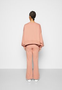 Sweatshirt oversized de tom rosa claro combinado com calças de fato largas da mesma cor, ambas feitas de um tecido suave, apresentando um corte descontraído e mangas com punhos.