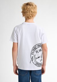 Bílý bavlněný tričko s krátkým rukávem, na zadní straně s velkým černým potiskem zobrazujícím "PETROL® IND." a "Miami Speed."