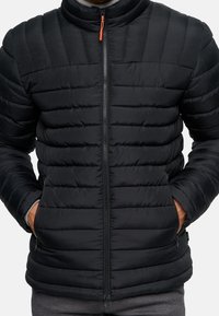 Schwarze gesteppte Daunenjacke mit hohem Kragen, Frontreißverschluss und Seitentaschen. Hat eine glatte Textur und einen kontrastierenden orangefarbenen Reißverschlussgriff.