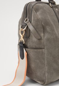 Šedá semišová kabelka se zapínáním na zip, s kovovým zlatým klipem a vícebarevným popruhem s oranžovými akcenty. Texturovaný, kompaktní design.