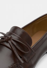 Καφέ δερμάτινο παπούτσι loafer με στρογγυλεμένη μύτη, διακοσμητικό κορδόνι φιογκάκι, ραφές στα πλάγια και γυαλιστερό, λείο φινίρισμα.