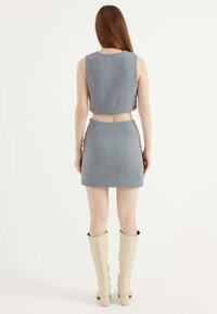 Grijs houndstooth crop top en mini rok set. Zachte stof, mouwloos ontwerp en hoge taille, gecombineerd met kniehoge beige laarzen.