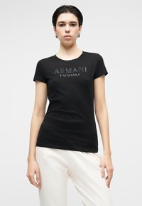 Melna kokvilnas T-krekls ar īsām piedurknēm, priekšpusē ar teksturētu sudraba krāsas "ARMANI EXCHANGE" logotipu, papildināts ar apaļu kakla izgriezumu.