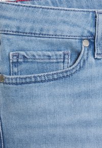 Jeans in denim azzurro chiaro con una piccola tasca frontale, dettagli in rivetti argentati e cuciture a contrasto lungo i bordi.
