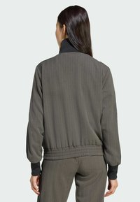 Tmavozelená rebrovaná bunda s vysokým golierom a elastickým lemom. Má kontrastné čierne manžety a voľný strih.