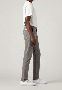 Pantaloni grigi in cotone con taglio dritto e tasche laterali, abbinati a una t-shirt bianca semplice e sneakers bianche.