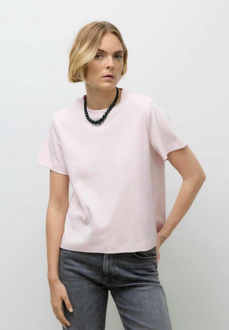 Lichtroze t-shirt met korte mouwen van zachte stof, met een ronde halslijn, gecombineerd met donkergrijze jeans en een zwarte kralenketting.