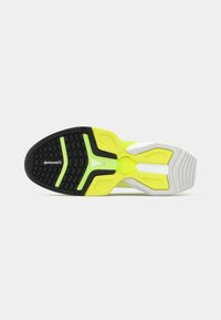 Εξωτερική σόλα παπουτσιού για τρέξιμο με μαύρη υφή από καουτσούκ στη βάση, λαμπερά κίτρινα στοιχεία στη μέση της σόλας και λευκό τμήμα στη φτέρνα με σχέδια πρόσφυσης.