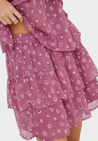 Gonna a strati con volant in un tessuto rosa chiaro, caratterizzata da un motivo geometrico in tonalità di rosa e bordeaux più scure. Vita elastica.