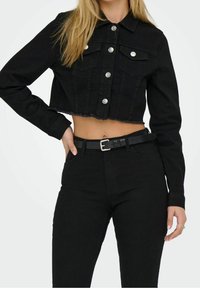 Black cropped denim jacket with a raw hem, silver button closures, and two chest pockets. Paired with high-waisted black pants and a black belt.