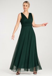 Maxi sukienka w ciemnozielonym kolorze, z dekoltem w kształcie litery V, dopasowaną górą z marszczeniami oraz przezroczystą warstwą. Przezroczyste ramiączka i zwiewny dół.