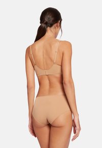 Nude bh med justerbare stropper og en glat overflade, parret med matchende nude trusser, der viser et sømløst design og minimal hardware.