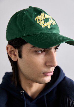 Casquette en coton vert avec un texte brodé jaune indiquant "Billionaire Boys Club". Comprend une visière courbée et une sangle ajustable à l'arrière.