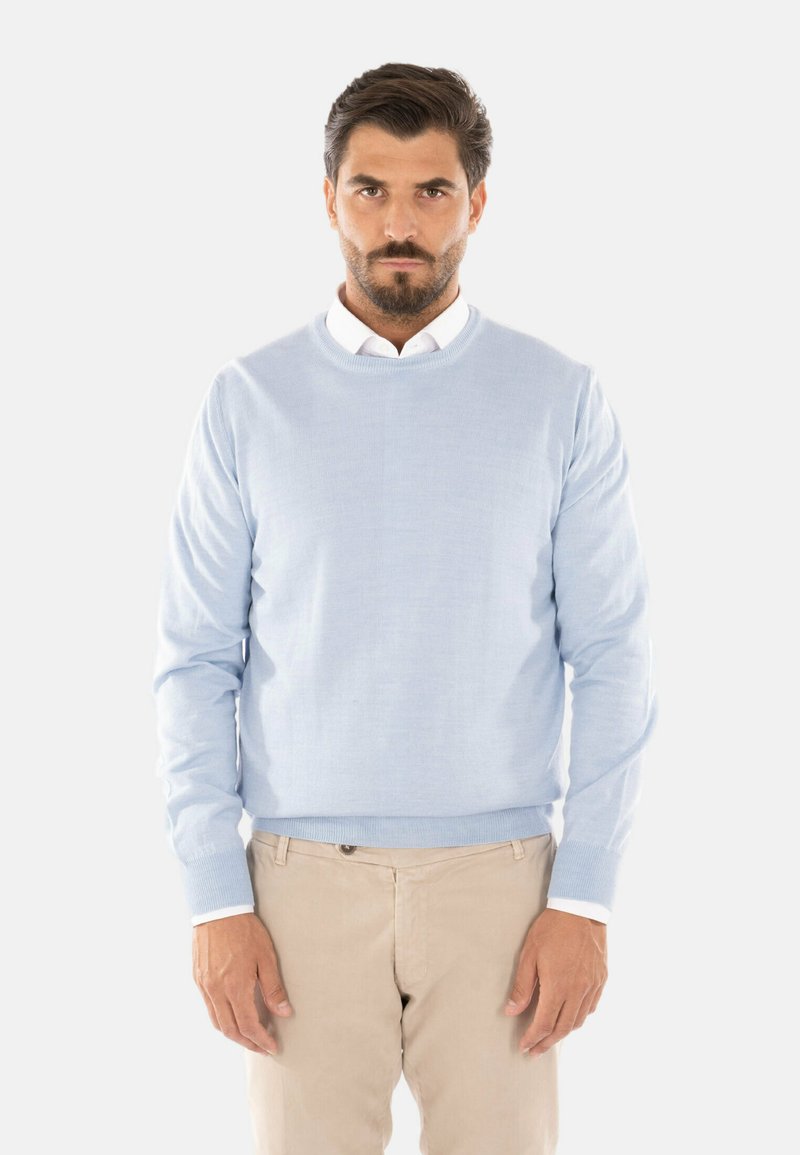 Maglione azzurro chiaro in tessuto a maglia, collo rotondo, maniche lunghe, abbinato a pantaloni color beige, con una camicia a colletto bianco sotto.