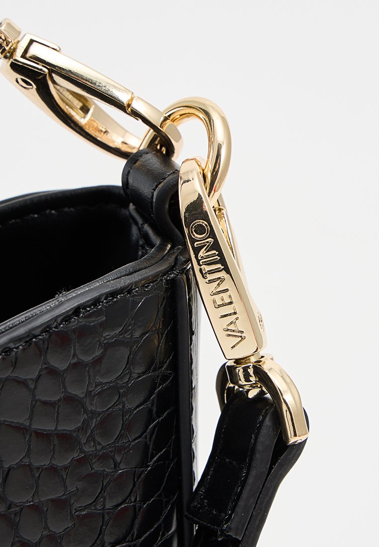 Schwarze Handtasche mit Krokodilprägung und glatter Textur, ausgestattet mit einem goldfarbenen Verschluss und einem Marken-Logoanhänger. Winklige Form mit strukturiertem Design.
