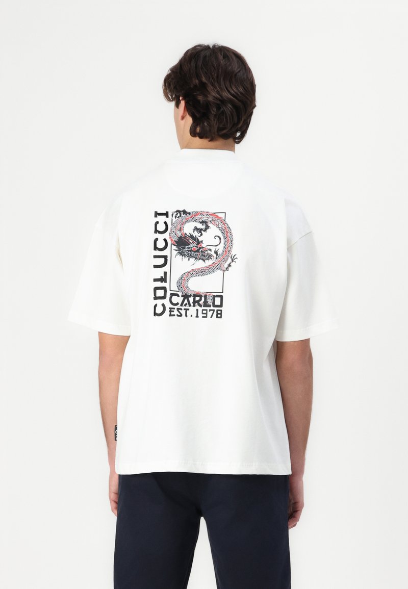 Vit bomull t-shirt med en färgglad drake grafik och text på baksidan. Avslappnad passform med rund hals och korta ärmar.