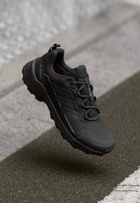 Schwarzer Sportschuh mit strukturiertem Obermaterial, drei seitlichen Streifen, runden Schnürsenkeln und einer robusten Sohle, die für Outdoor-Aktivitäten entworfen wurde.