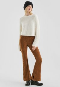 Fluffy witte cropped trui, bruine flared broek met zijsplitten, zwarte gebreide beanie en zwarte enkellaarsjes. Zachte textuur overal.