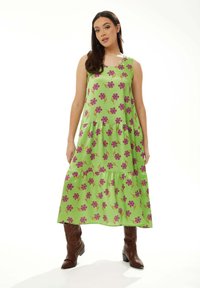 Green floral maxi dress featuring purple flower patterns, tiered design, and spaghetti straps. Paired with brown cowboy boots.