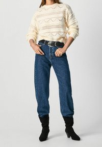 Chunky creamfärgad stickad tröja med öppna mönster, kombinerad med högmidjade blå denimjeans och svarta klackade ankelstövlar.