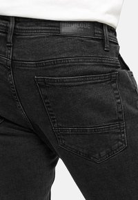 Svarte denim bukser med en tettsittende design, med en baklomme og et merket lærpatch ved midjen, glatt tekstur og slitesterk søm.