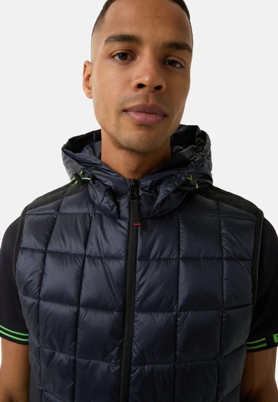 Marineblaue Steppweste mit einem gesteppten Muster, Reißverschluss und Kapuze. Mit grünen Akzenten und schwarzen Stoffdetails an den Schultern.