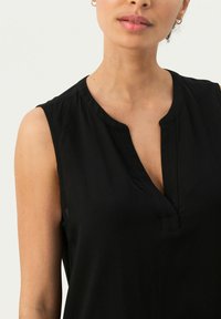 Top negro sin mangas con diseño en forma de V, hecho de una tela suave. Presenta un acabado limpio con costuras mínimas y sin acentos visibles.