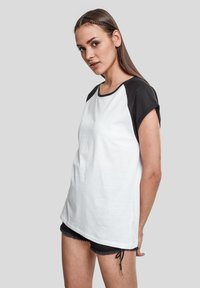 Camiseta de manga corta blanca y negra con cuello redondo, que presenta un corte holgado y material de algodón suave, combinada con pantalones cortos negros.