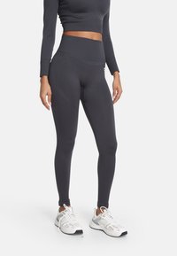 Čierne legíny s vysokým pásom vyrobené z hladkej, elastickej tkaniny. Majú priliehavý strih a bezšvové akcenty, ktoré vedú po stranách.