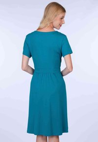 Tee-farbendes kurzes Kleid mit kurzen Ärmeln, rundem Ausschnitt, tailliertem Schnitt und ausgestellt Rock. Glatte Textur, knielang und mit gerafftem Detail im Rücken.