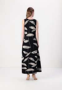 Svart maxiklänning med vita bladmönster. Ärmlös design, rak silhuett och en slät textur. Klara klackar synliga längst ner.