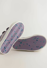 Paarse sneakers met witte rubberen zolen. De zool heeft een zigzagpatroon met teal en blauwe accenten. Verstelbare riem voor het vastmaken.