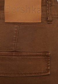 Bruna denimbyxor med en texturerad tyg, en bakficka och en märkesläderetikett sydd i midjan.