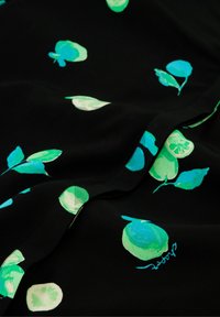 Schwarzer Stoff mit einem lebhaften Muster aus grünen und türkisfarbenen Blättern sowie kreisförmigen Formen, mit einer weichen Textur und sichtbaren Nähdetails.
