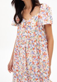Robe fleurie à coupe fluide, manches courtes volantées, décolleté en V, motif de fleurs multicolores sur fond clair, et détail de bouton sur le devant.