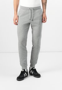 Gray sweatpants with elastic waistband and drawstring. Tapered fit with side pockets and ribbed cuffs. Paired with black sneakers.