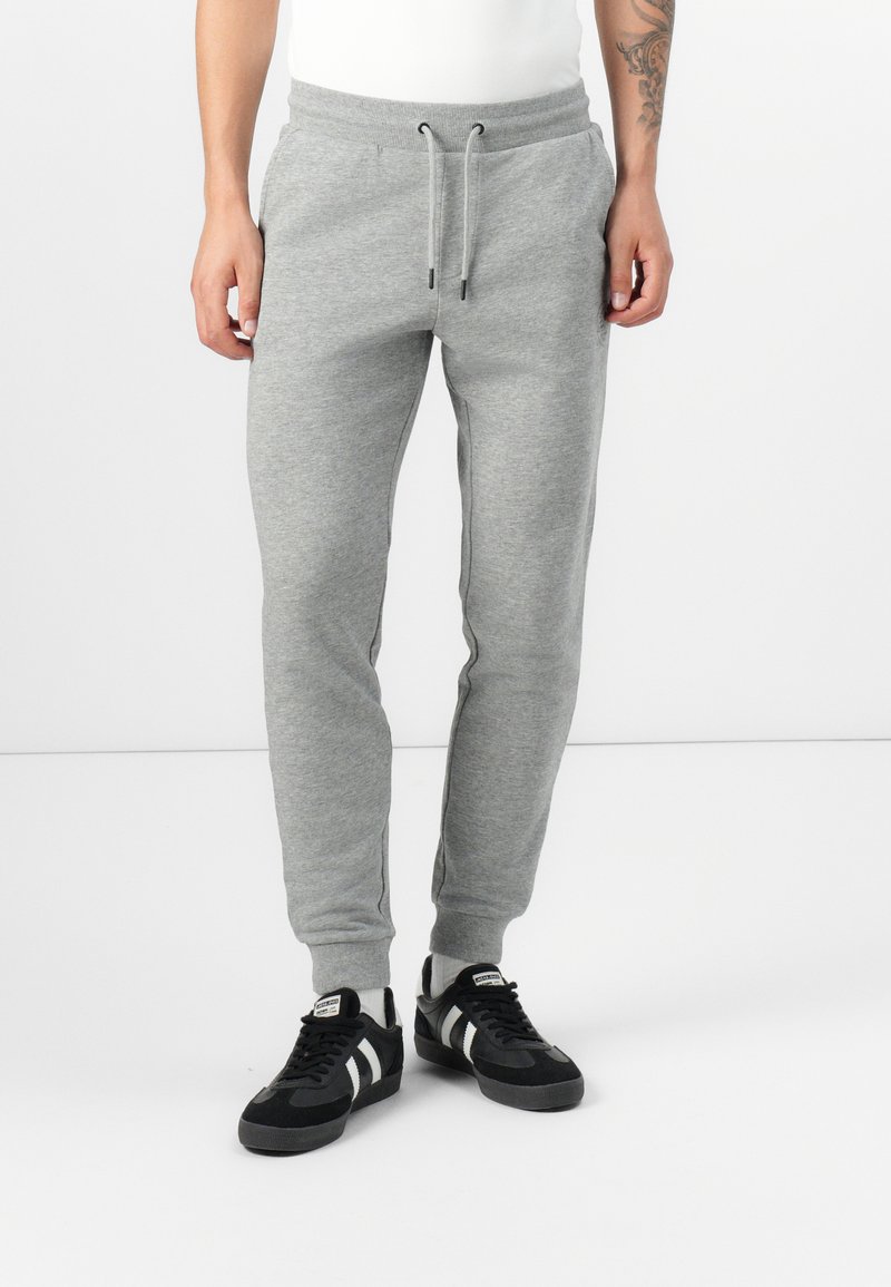 Gray sweatpants with elastic waistband and drawstring. Tapered fit with side pockets and ribbed cuffs. Paired with black sneakers.