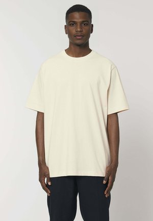 Crème kleurige oversized t-shirt van katoen, met een ronde hals en korte mouwen, gedragen met donkere broeken. Gelaagd weefsel zonder patronen.