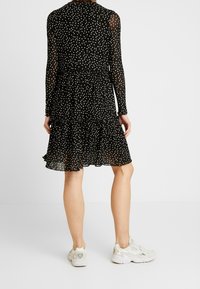 Musta, pitkähihainen mekko valkoisilla pilkuilla, kerrosmainen ripsuhaara, läpikuultava kangas, yhdistettynä vaaleisiin urheilukengiin.